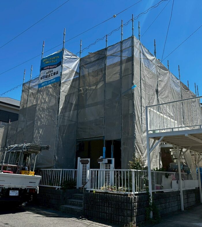屋根リフォーム工事のため住宅全体に足場と飛散防止ネットを設置した様子。安全対策を徹底して工事を開始する現場。