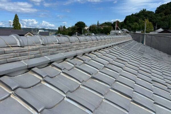 青空の下、瓦屋根の葺き直しと陸棟交換が完了した住宅の屋根全景。真っ直ぐ美しく積み直された棟瓦と、整然と並んだ平瓦が仕上がりの良さを示している施工後の様子