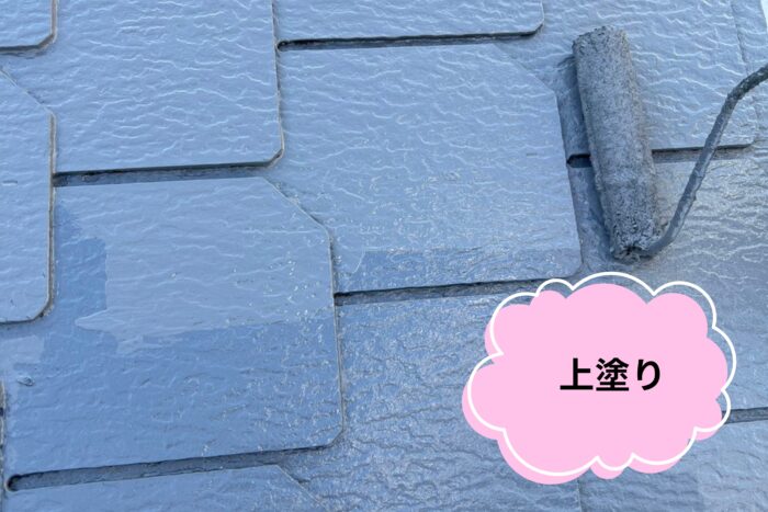 スレート屋根にローラーでグレーの塗料を均一に塗布している上塗り作業の近接写真