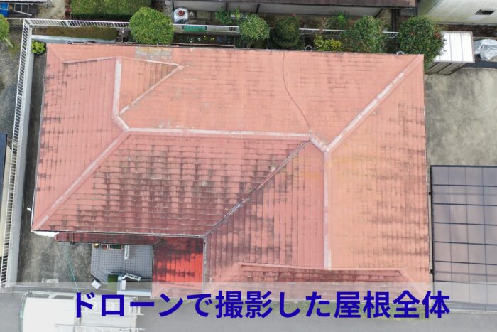 ドローン空撮で屋根全体を真上から撮影した写真。カラーベスト屋根全体に色あせ・黒ずみ・コケが広がり、特に下屋部分では塗膜の剥がれが進行している様子が確認できる。