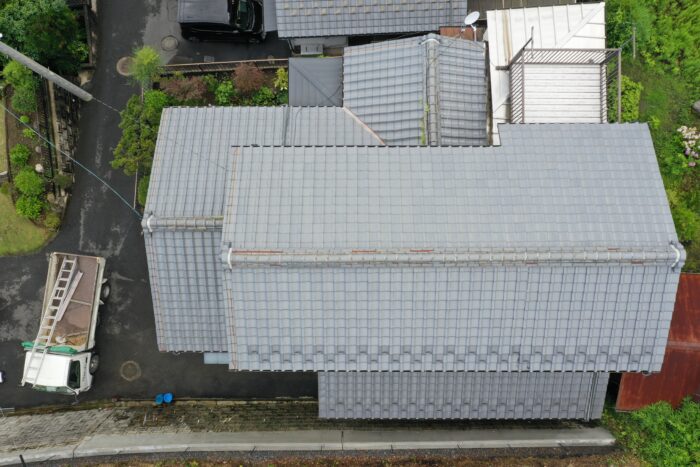 瓦屋根全体のドローン撮影。棟のゆがみと錆びた谷板金が確認できる。