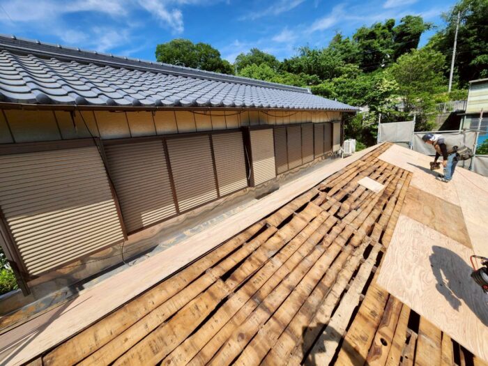 葺き土と瓦を撤去した後の屋根で、既存下地の上から構造用合板を増し張りして補強している葺き替え工事の様子