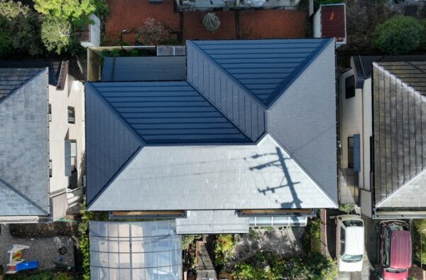 多治見市市之倉町で実施した屋根葺き替え工事・雨樋交換工事の施工後をドローンで撮影。新しい屋根材で美しく仕上がり、屋根全体の防水性・耐久性が向上した住宅の全景です。